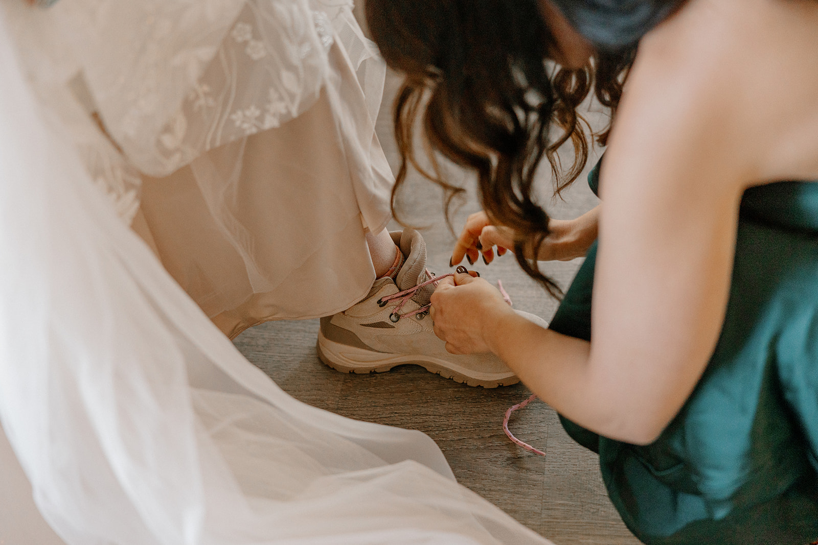 Bridesmaid helping bride put on hiking boots on bride before Arizona elopement