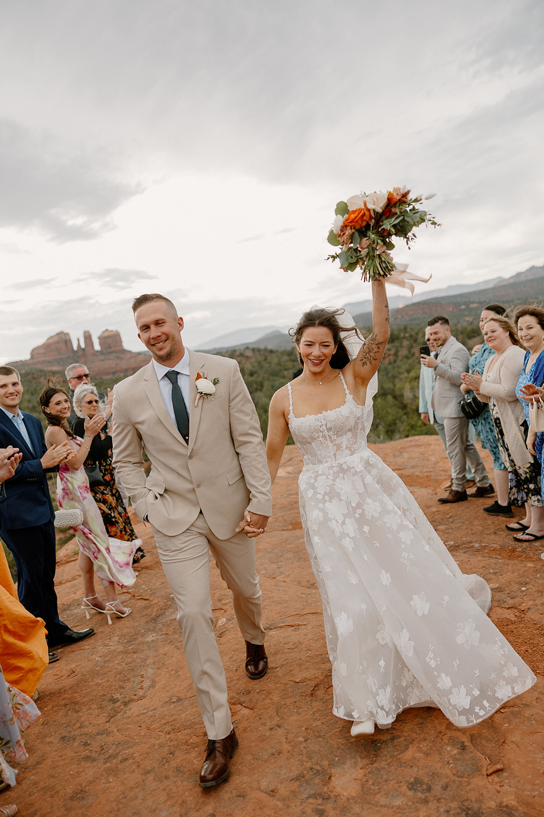 Bride triumphantly raising her bouquet as she and her groom walk back down the red rock aisle at their Arizona elopement.