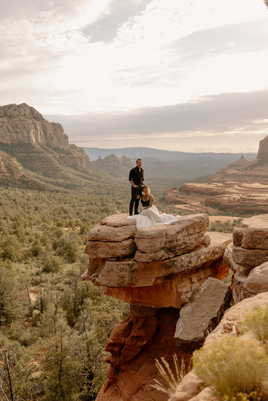 Newlyweds in edgy black and white wedding attire standing on a stacked boulder with sweeping canyon views