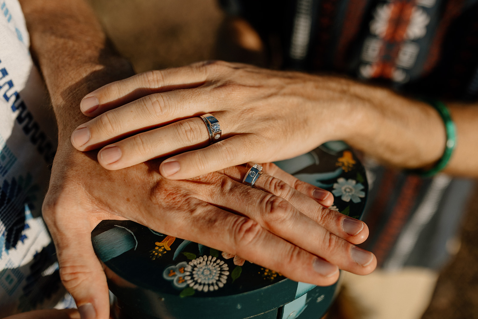 Two hands with matching gemstone rings resting on a hand-painted box during an outdoor ceremony