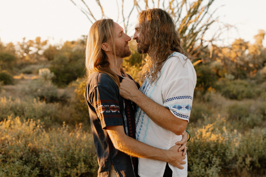 Two grooms in embroidered shirts sharing an intimate look in the warm desert light

