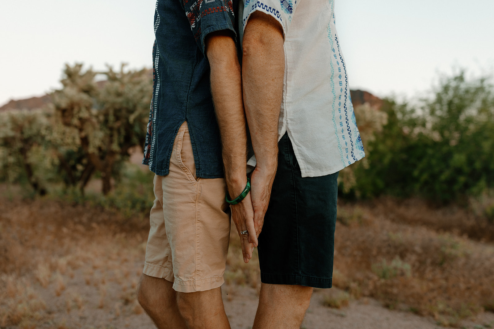 Close-up of couple in shorts and patterned shirts holding hands gently between their sides

