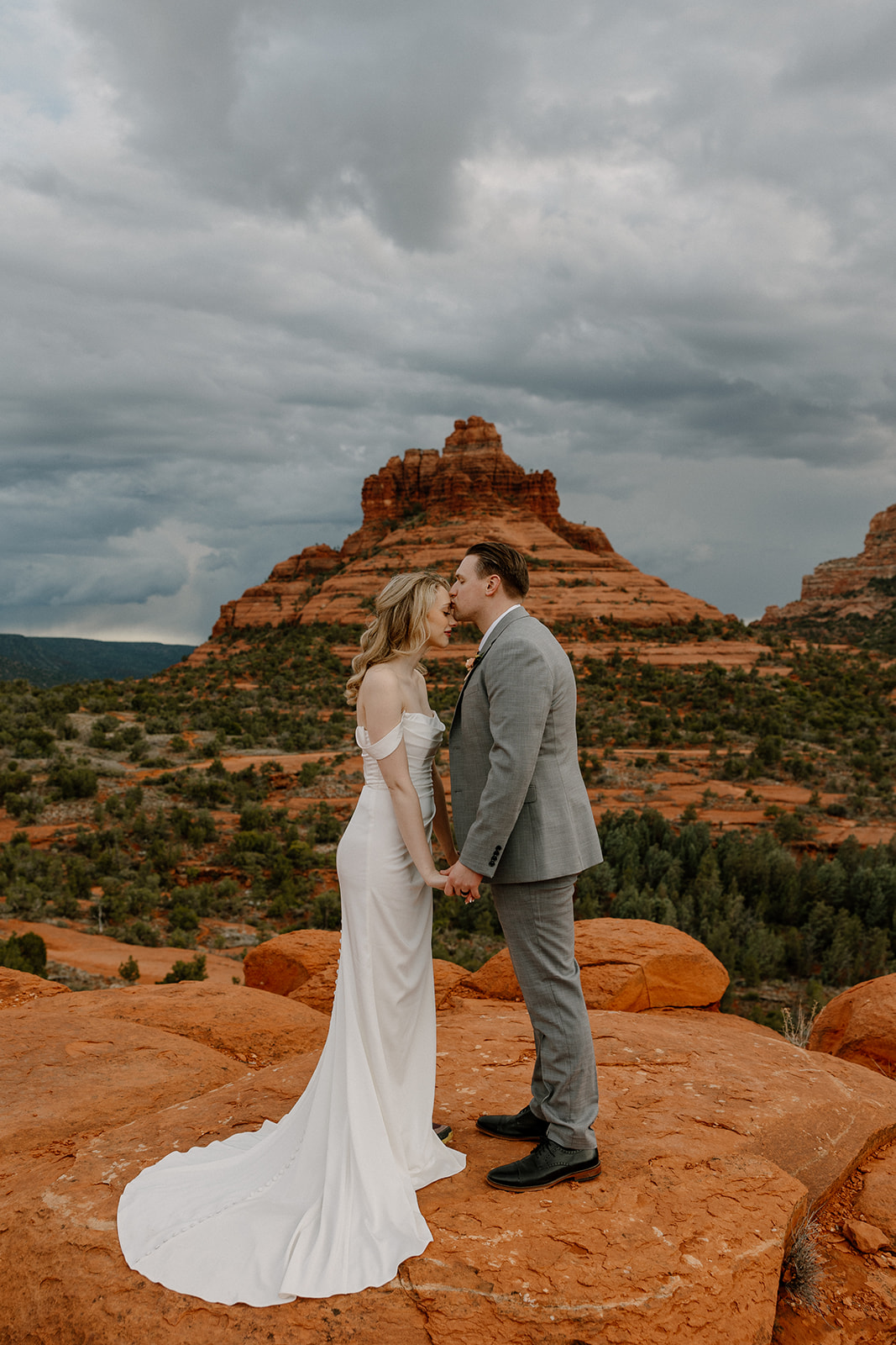 Couple kissing on red rocks in Sedona, bride in sleek off-the-shoulder elopement dress.