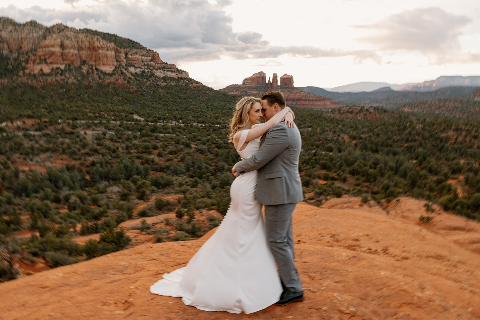 Couple embracing on red rock with arms around one another after intimate elopement