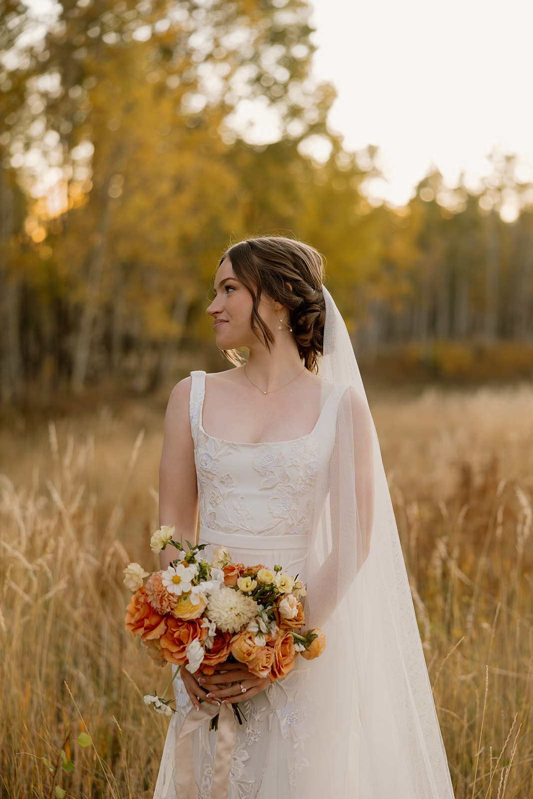 Bride in embroidered elopement dresses with veil standing in golden autumn field.