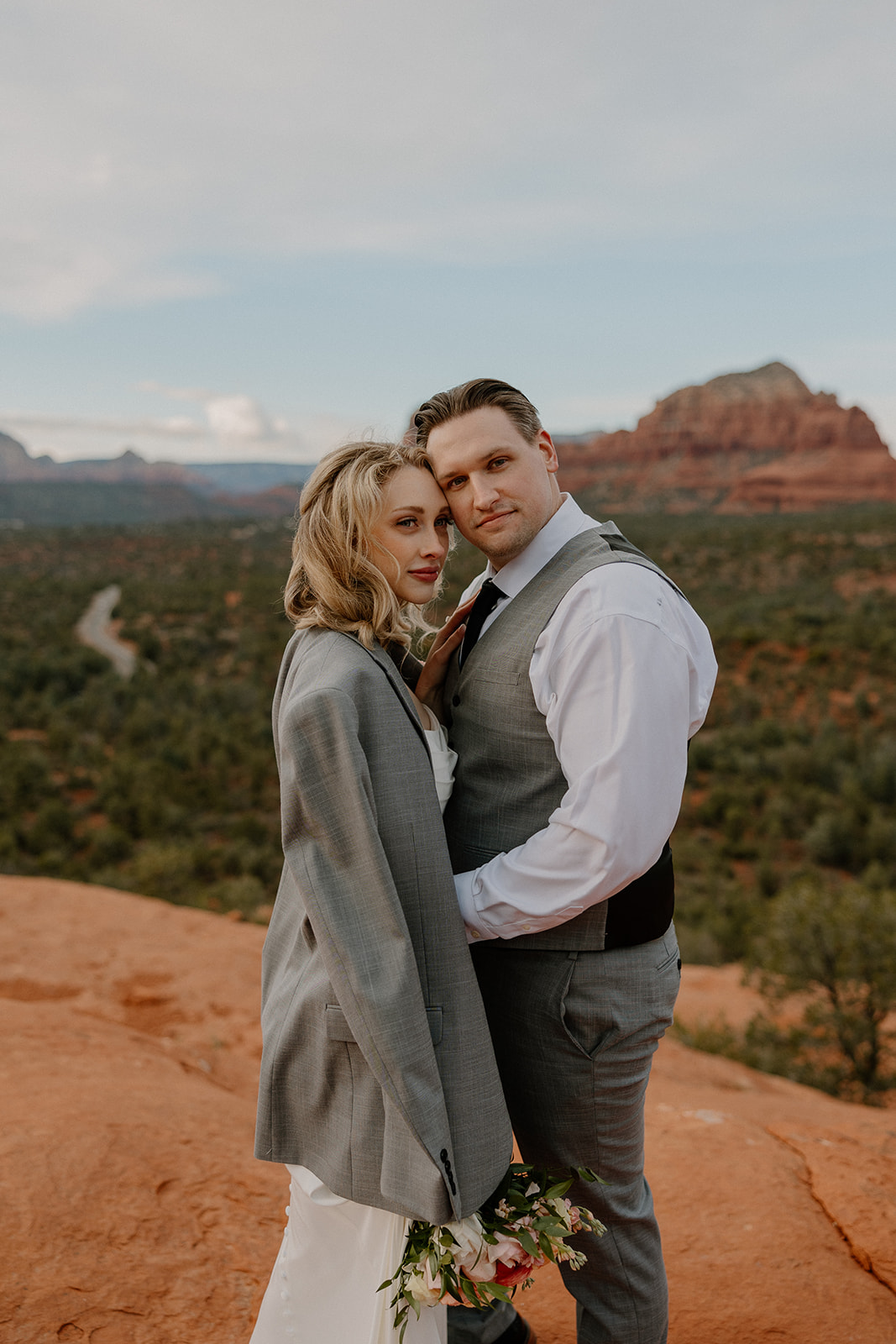 Stylish twist on groom wedding attire with a gray vest and slacks, as the bride wears his blazer for a laid-back desert portrait.