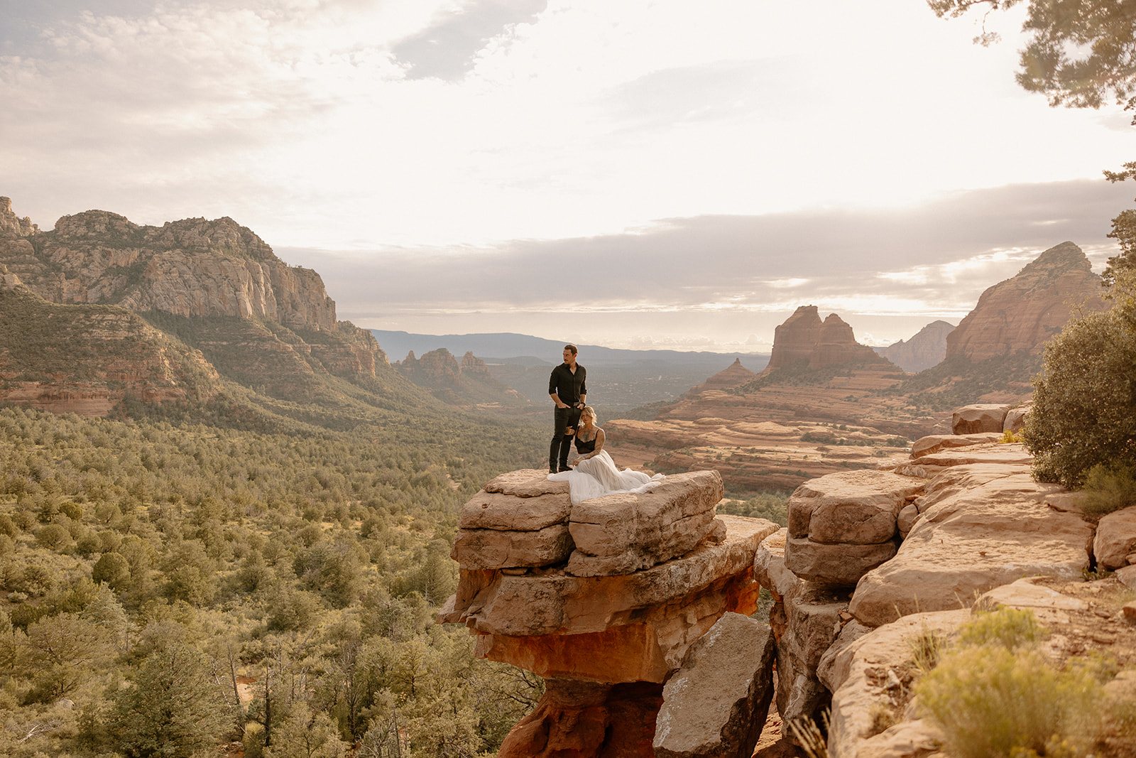 Adventurous groom wedding attire in an all-black suit, standing with his bride on a dramatic cliffside in Sedona with sweeping canyon views.
