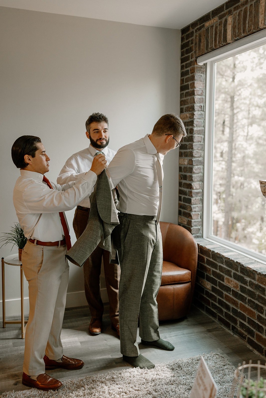 Getting ready moment as the groom is helped into his green wedding suit by his groomsmen—classic groom wedding attire prep.