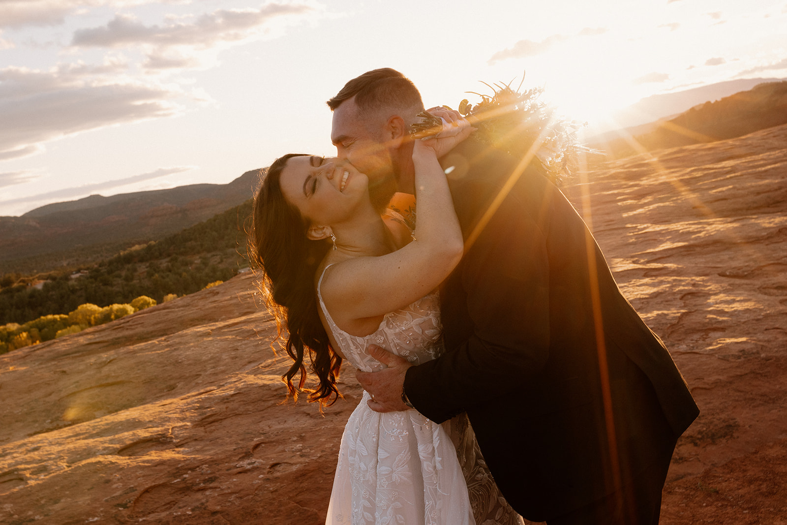 Sunlight wraps around a couple sharing a kiss in the desert, the sky blushing behind them—showing what is the best time of day to elope for that golden, cinematic glow.