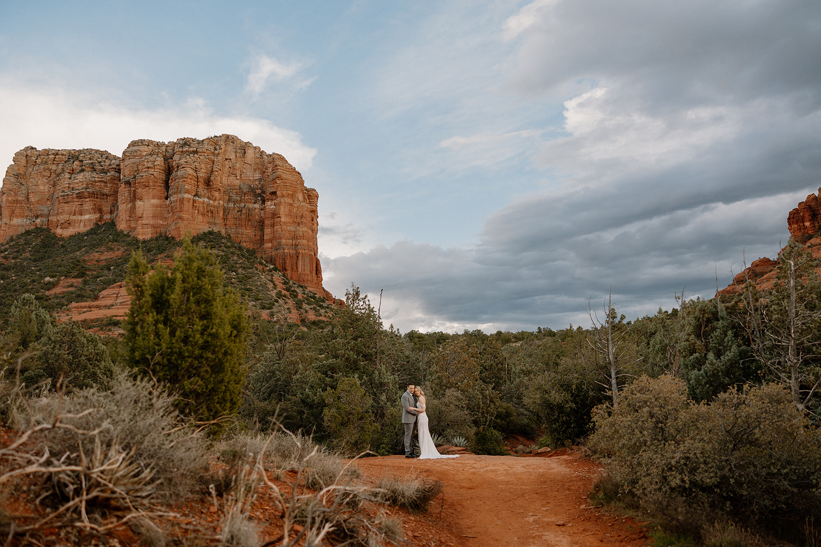 Bride and groom embrace in front of Bell Rock in Arizona featuring incredibly beautiful trees and red rocks throughout