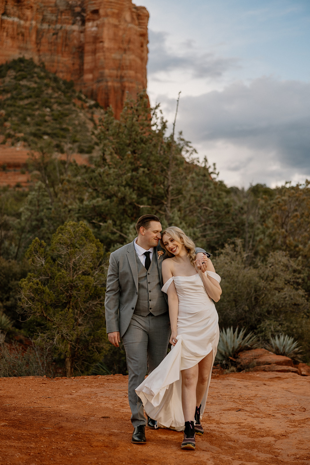 Bride and groom walking together as groom as arm around bride and she walks while wearing black boots 