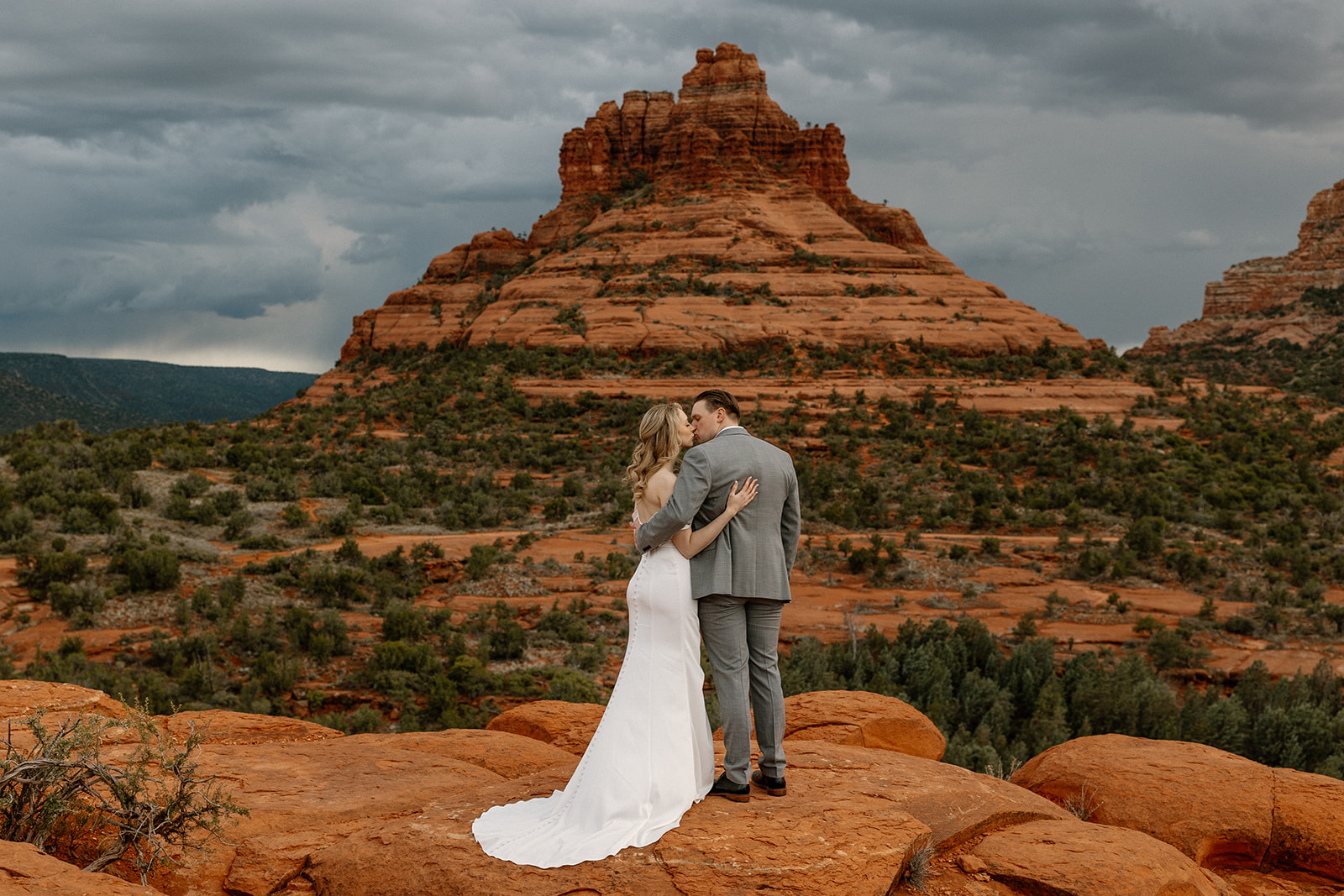 Bride and groom embrace on the red rocks of Sedona as moody clouds roll in—capturing the quiet before the storm.