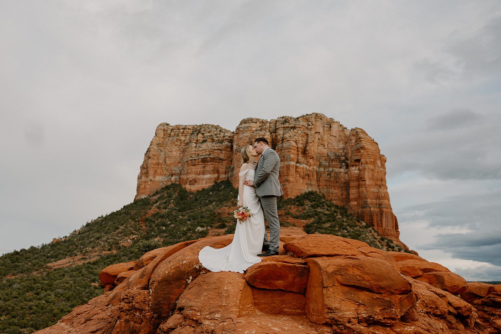 Bride and groom on top of rocky red mountain in Arizona kiss 