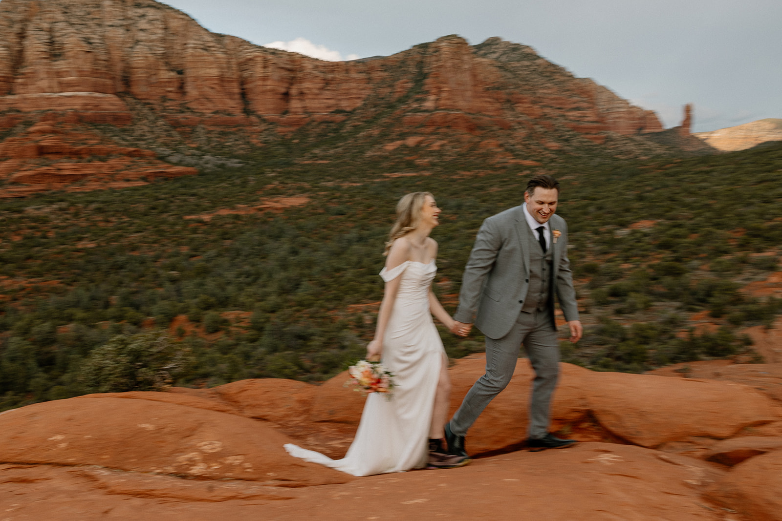 Artistic photo with blurred results of bride and groom running across deep red rocks after intimate Sedona elopement ceremony proving what is the best time to elope