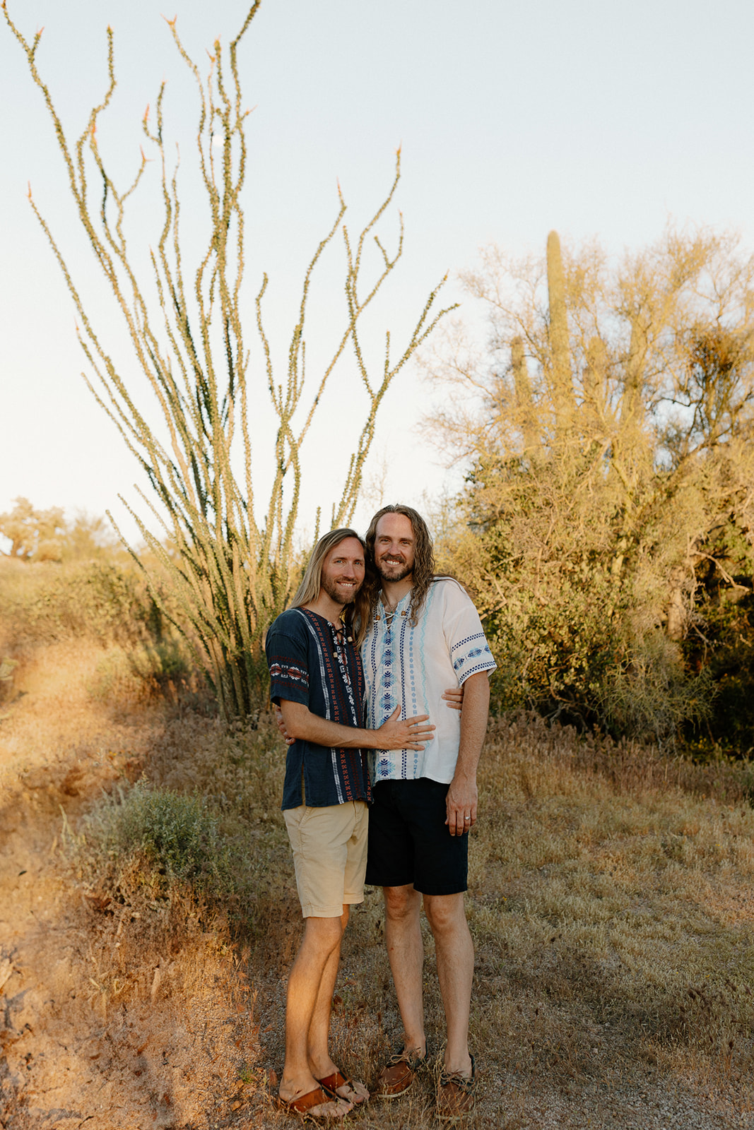Two grooms in casual elopement attire embrace after Sedona desert elopement at sunset