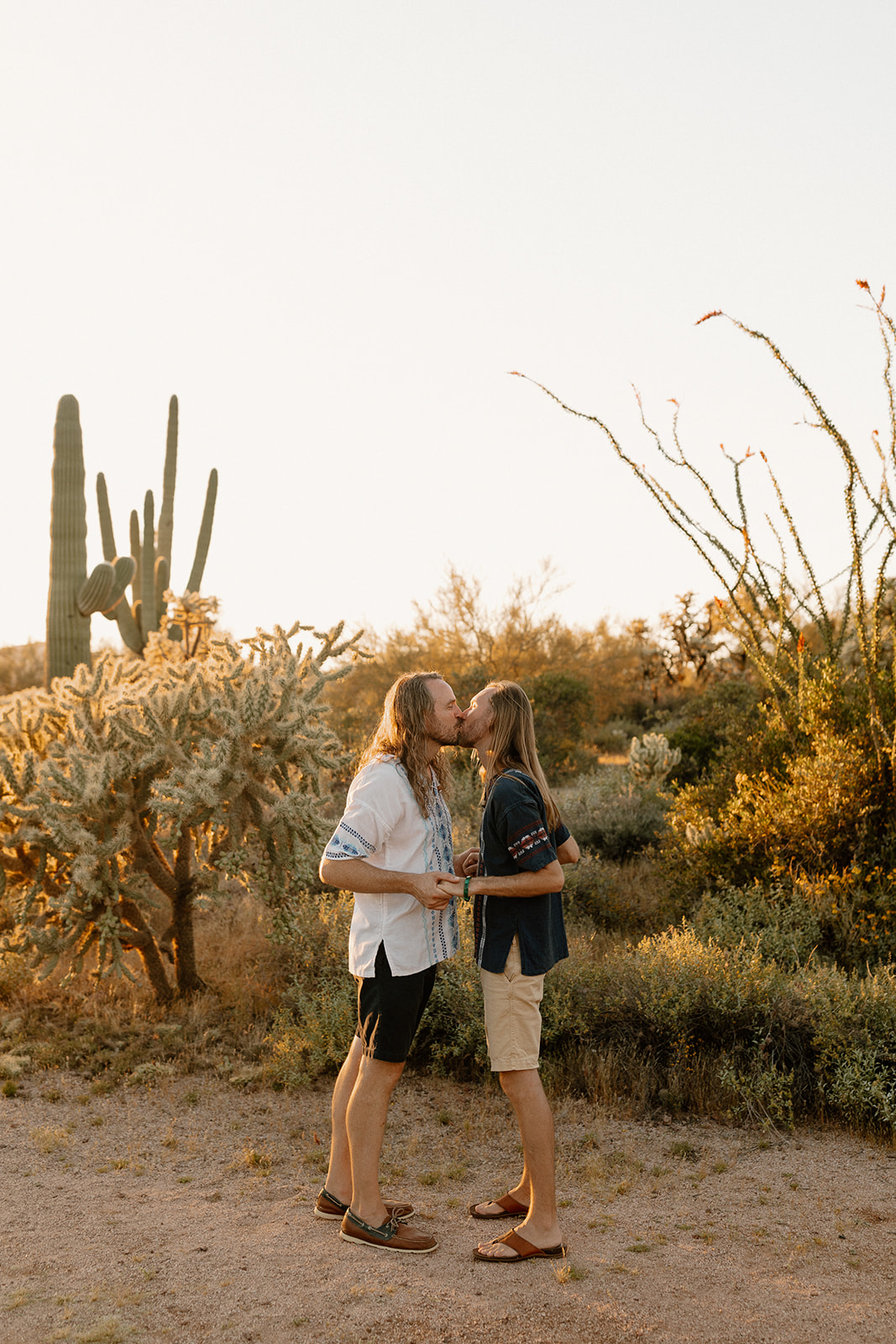Golden sunlight kisses this desert elopement as two grooms share a quiet moment surrounded by cacti—an example of what is the best time of day to elope for soft, warm tones.