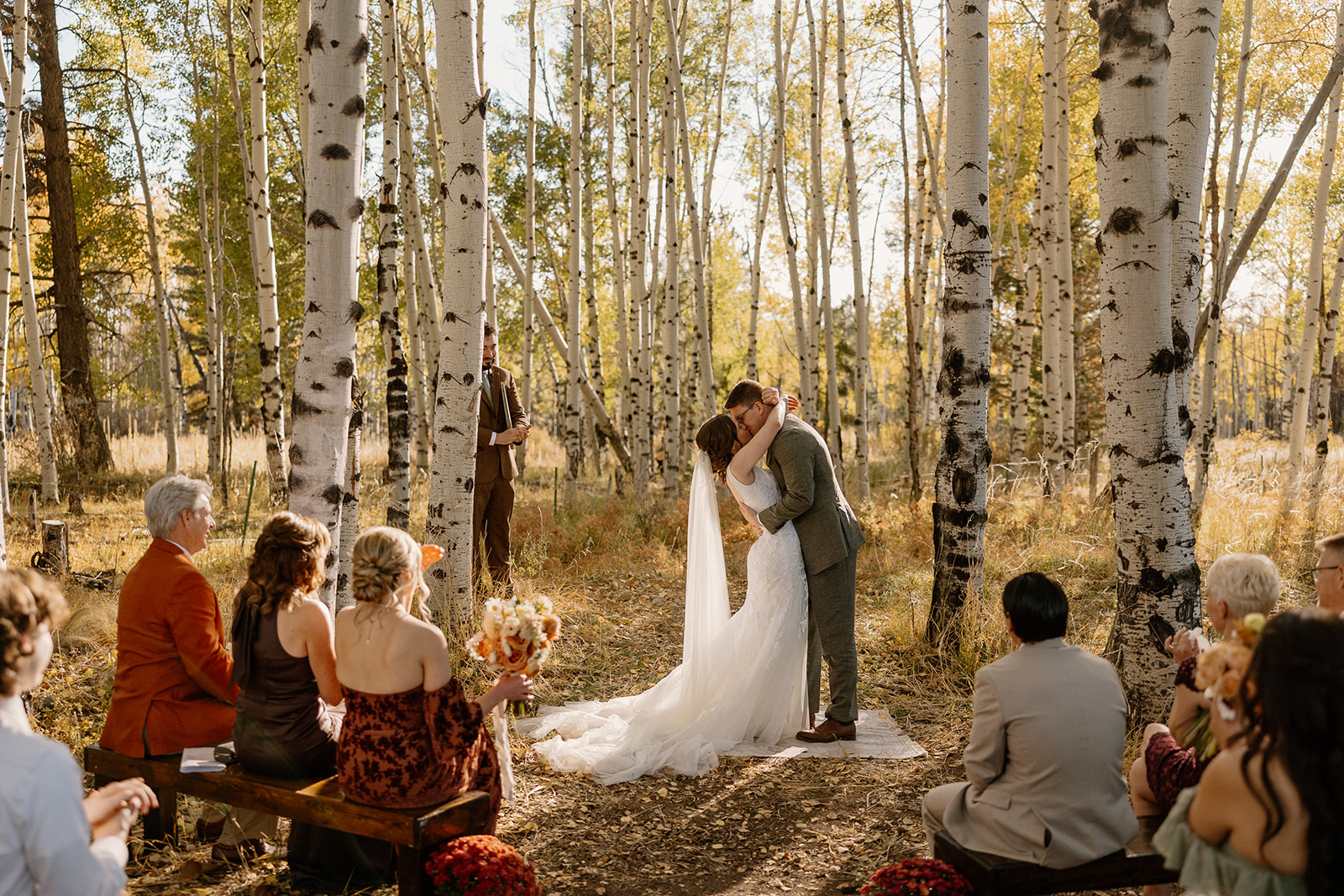 A joyful first kiss as newlyweds beneath golden aspens—dreamy afternoon light filters through the trees, making this the answer to what is the best time of day to elope in the woods.