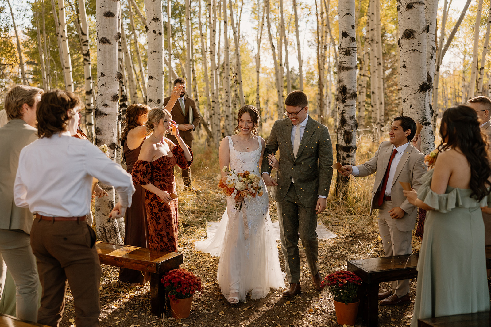 Newly married couple walks through golden aspens, surrounded by cheers from loved ones—this late-afternoon glow shows what is the best time of day to elope in the forest.