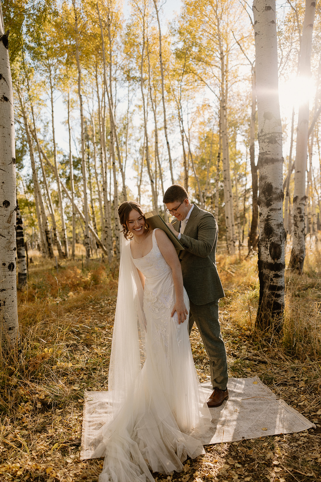 Bride laughs joyfully as groom uses her back to sign their marriage license. The sun peeking through the trees proves what time is the best to elope