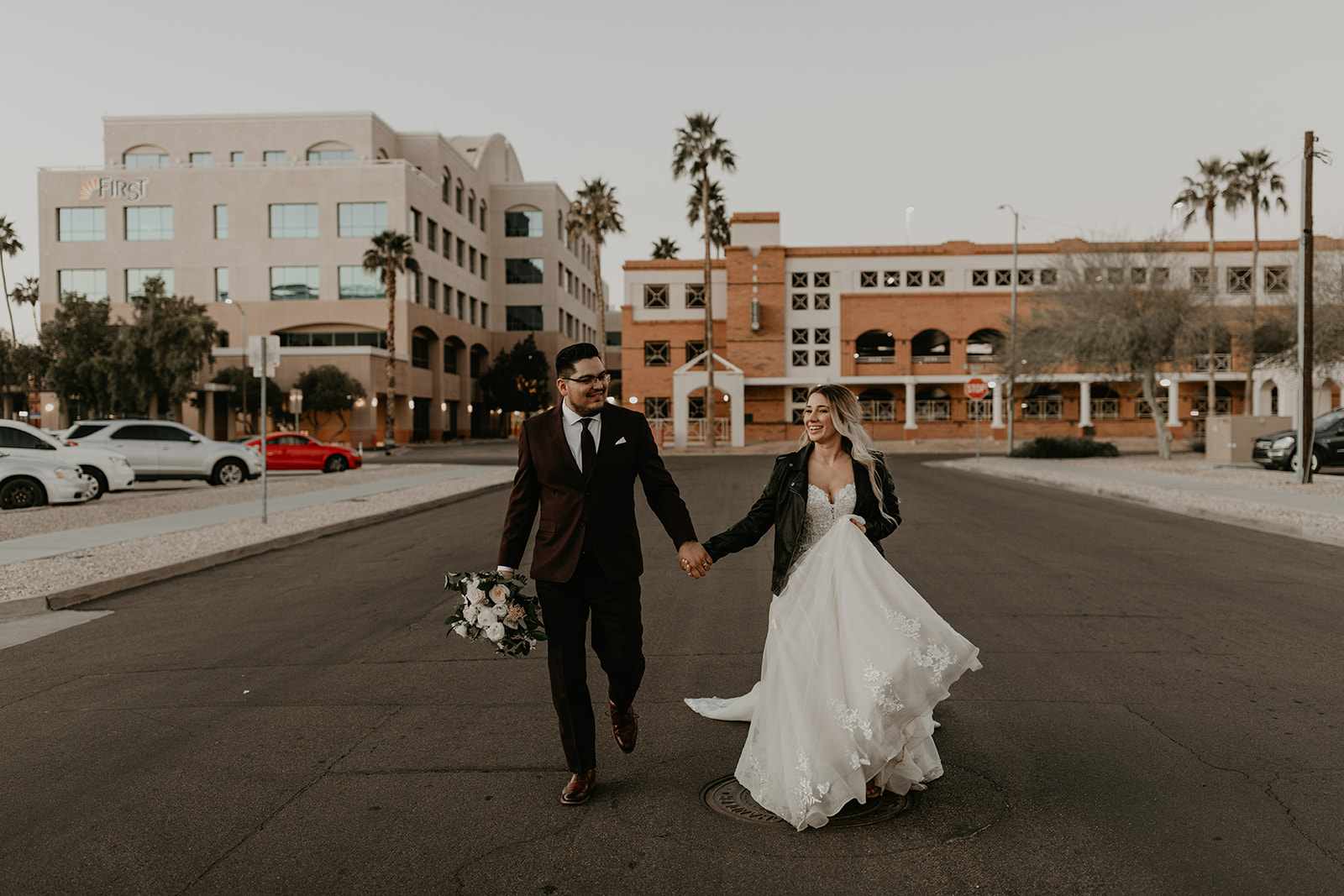 Bride and groom walking hand-in-hand through downtown Chandler near SoHo63, with city buildings and palm trees in the background.