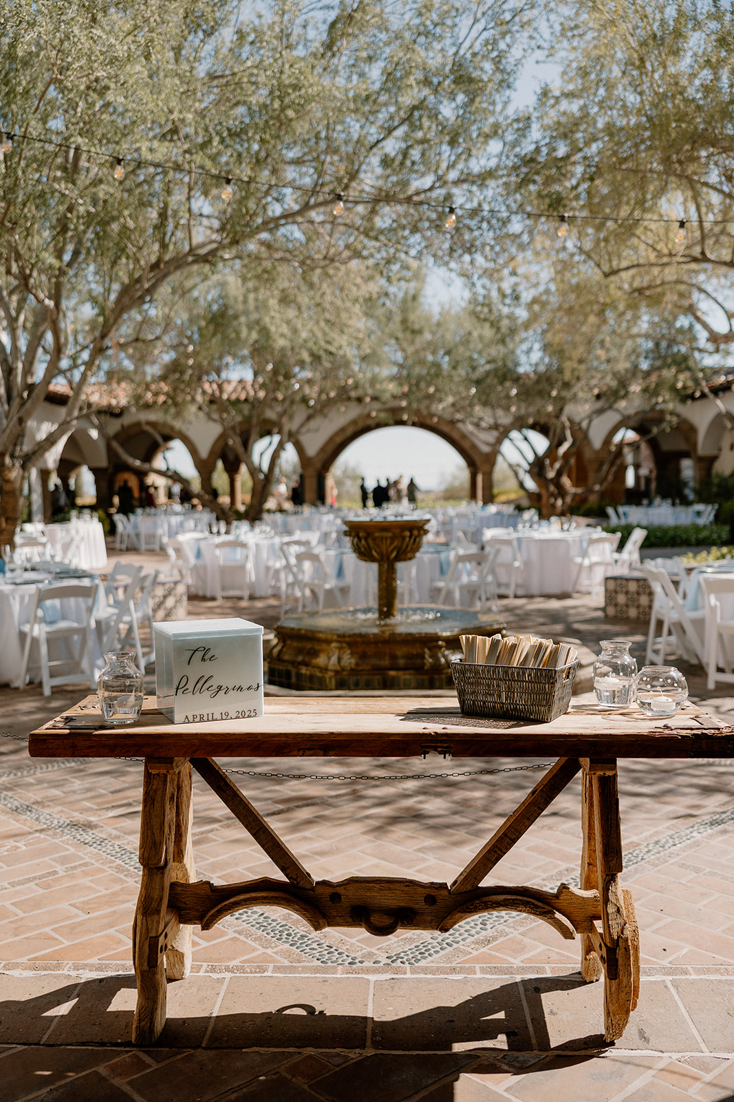 A rustic wooden welcome table sits in front of the courtyard fountain at Blackstone Country Club, with personalized signage and guest cards.
