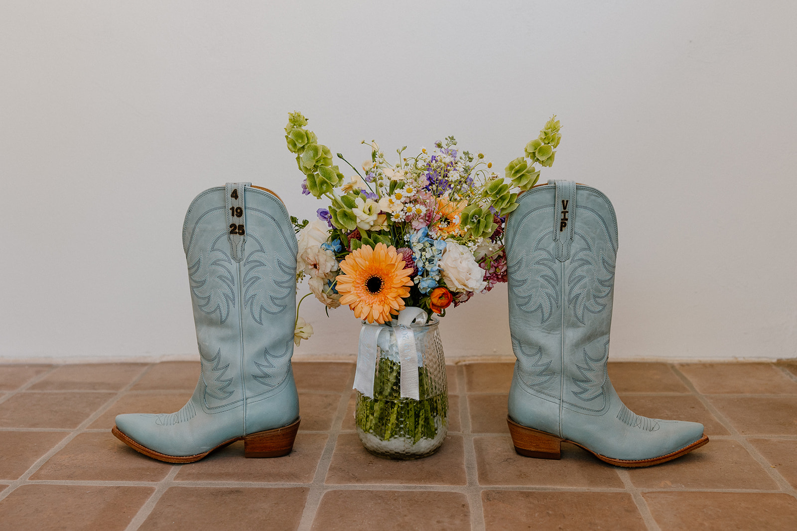 Powder blue cowboy boots frame a wildflower bridal bouquet in a mason jar—playful, personal, and full of Arizona charm.