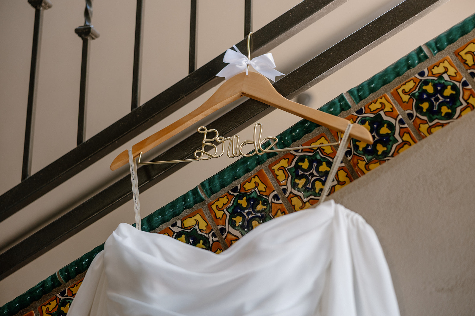A close-up of the wedding dress on a gold ‘bride’ hanger, with colorful Spanish tile accents in the background.