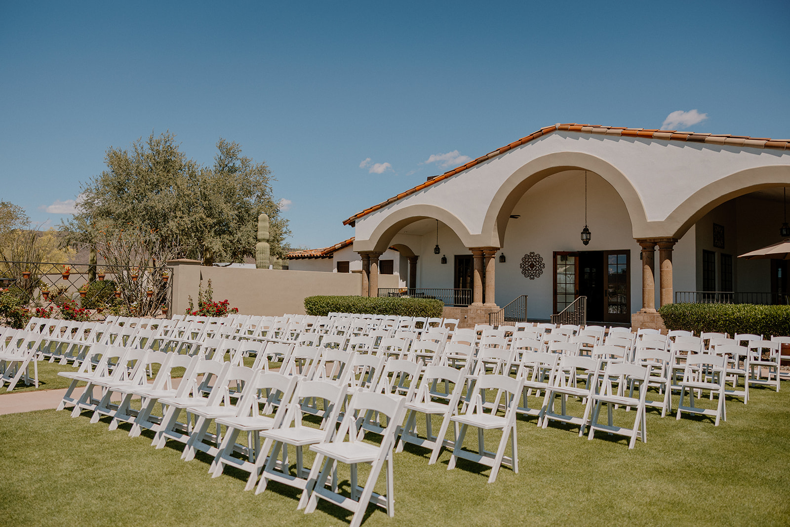 Rows of white ceremony chairs set against the Spanish-inspired arches at Blackstone Country Club under a bright blue sky.