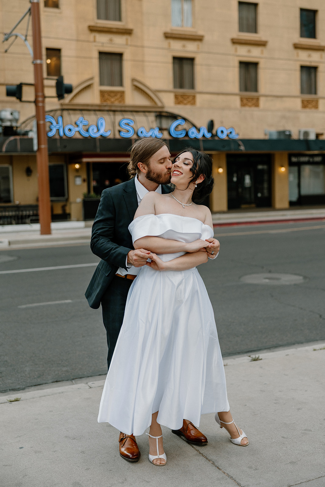 Bride and groom wrapped in a soft embrace on the street, the vintage hotel sign glowing behind them.