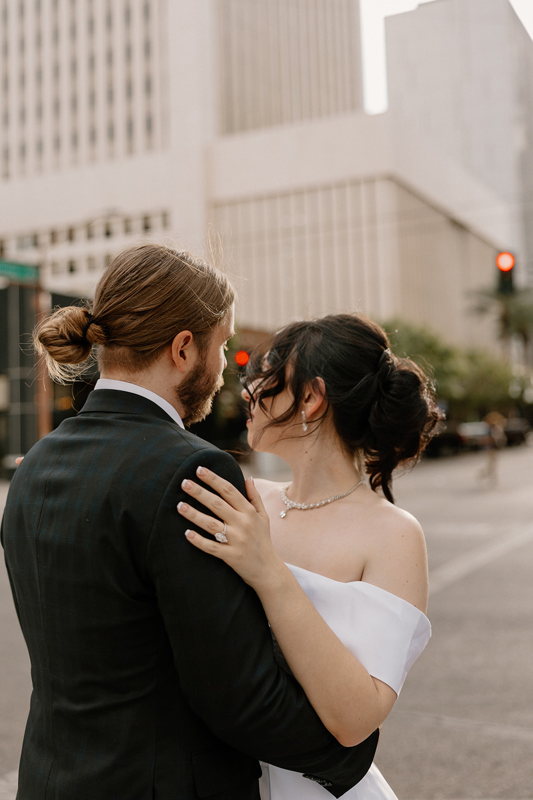 Couple holding each other and softly leaning in on a downtown street corner, surrounded by modern buildings.