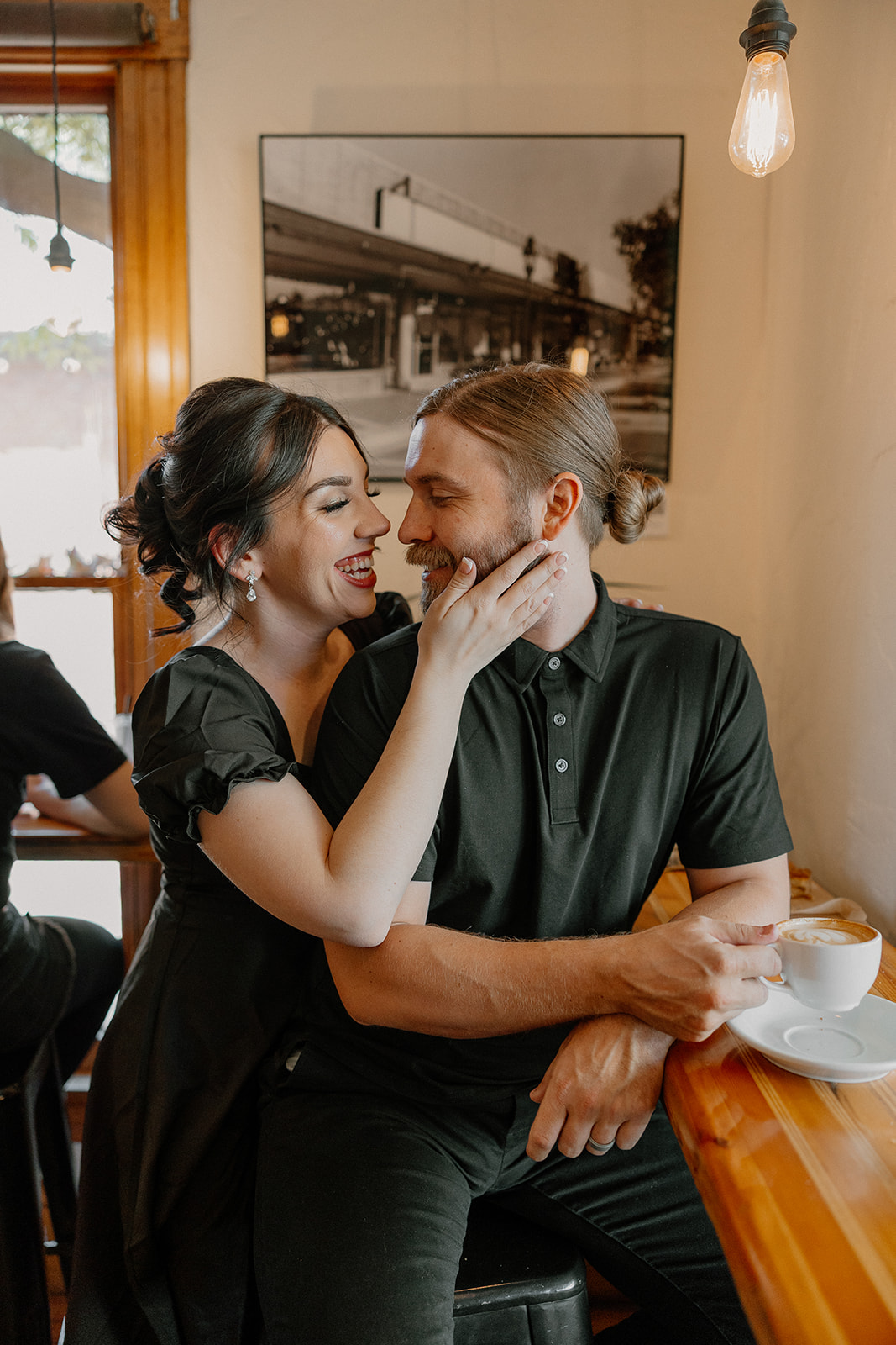 Woman smiling and touching her partner’s face while he holds a cappuccino at the bar of a cozy café.