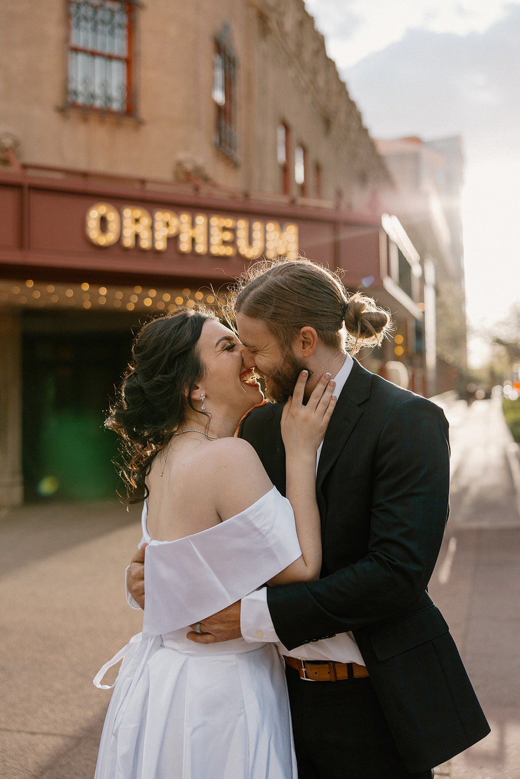 Couple laughing and holding each other as the sun sets behind them under the historic Orpheum sign.
