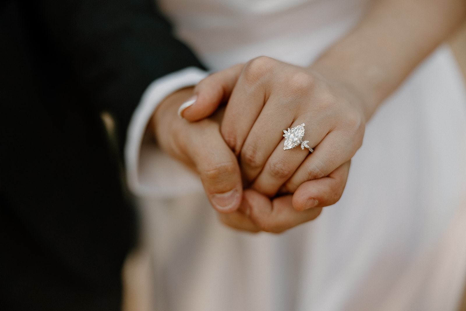 Detail shot of hands gently clasped, with a marquise engagement ring front and center.