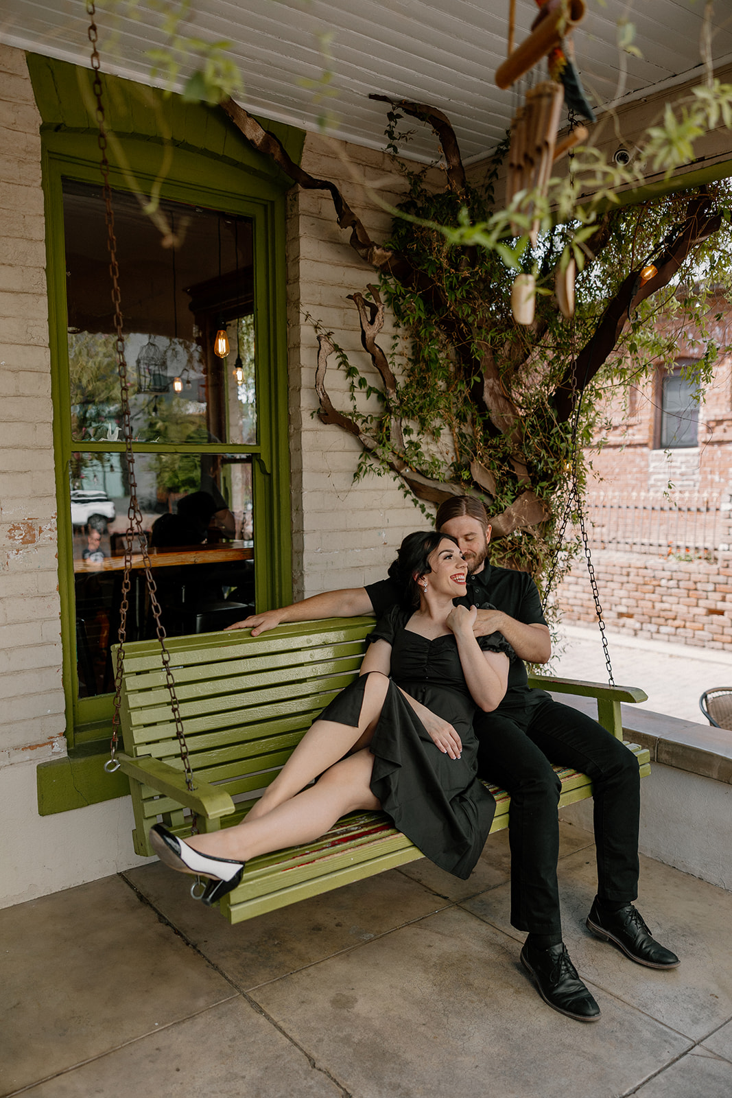 Couple relaxing on a green porch swing outside a local café — a cozy setting for their coffee shop engagement photos.