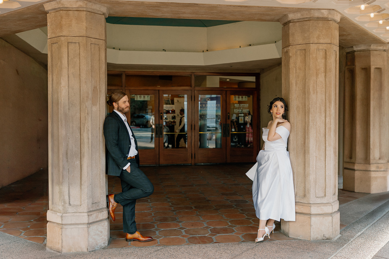 Engaged couple posing at a historic theater entrance, leaning casually against stone columns with vintage charm.