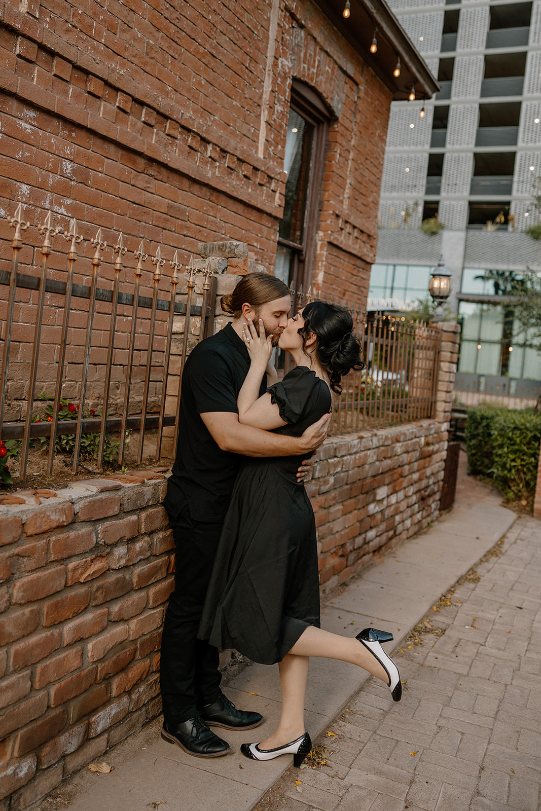 Couple sharing a romantic moment beside a red brick wall in an urban setting.