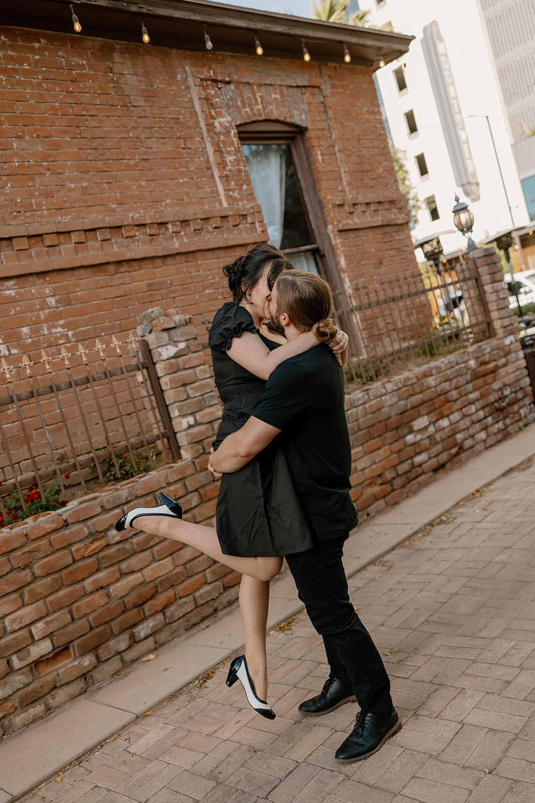 Groom lifting his fiancée in a tight hug during their coffee shop engagement session near a red brick alley.