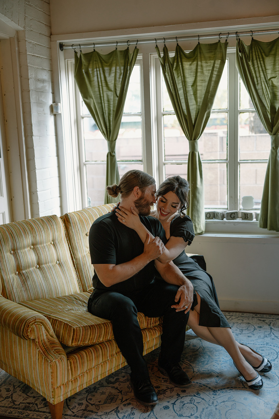 Couple sharing a sweet laugh on a mustard-striped couch during their coffee shop engagement photos.
