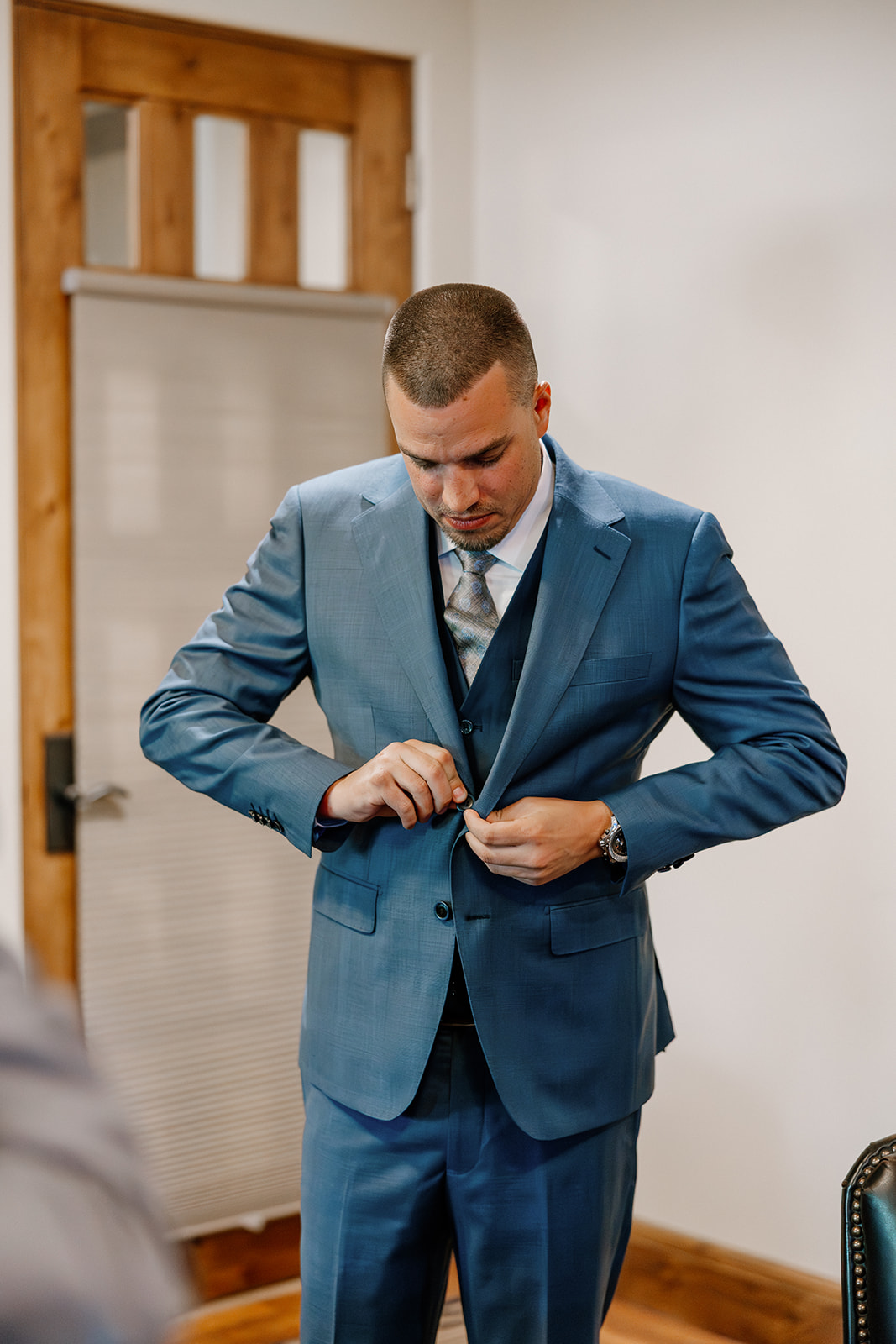 The groom buttons his jacket in the getting-ready suite, looking focused and composed before heading to Blackstone Country Club’s ceremony space.