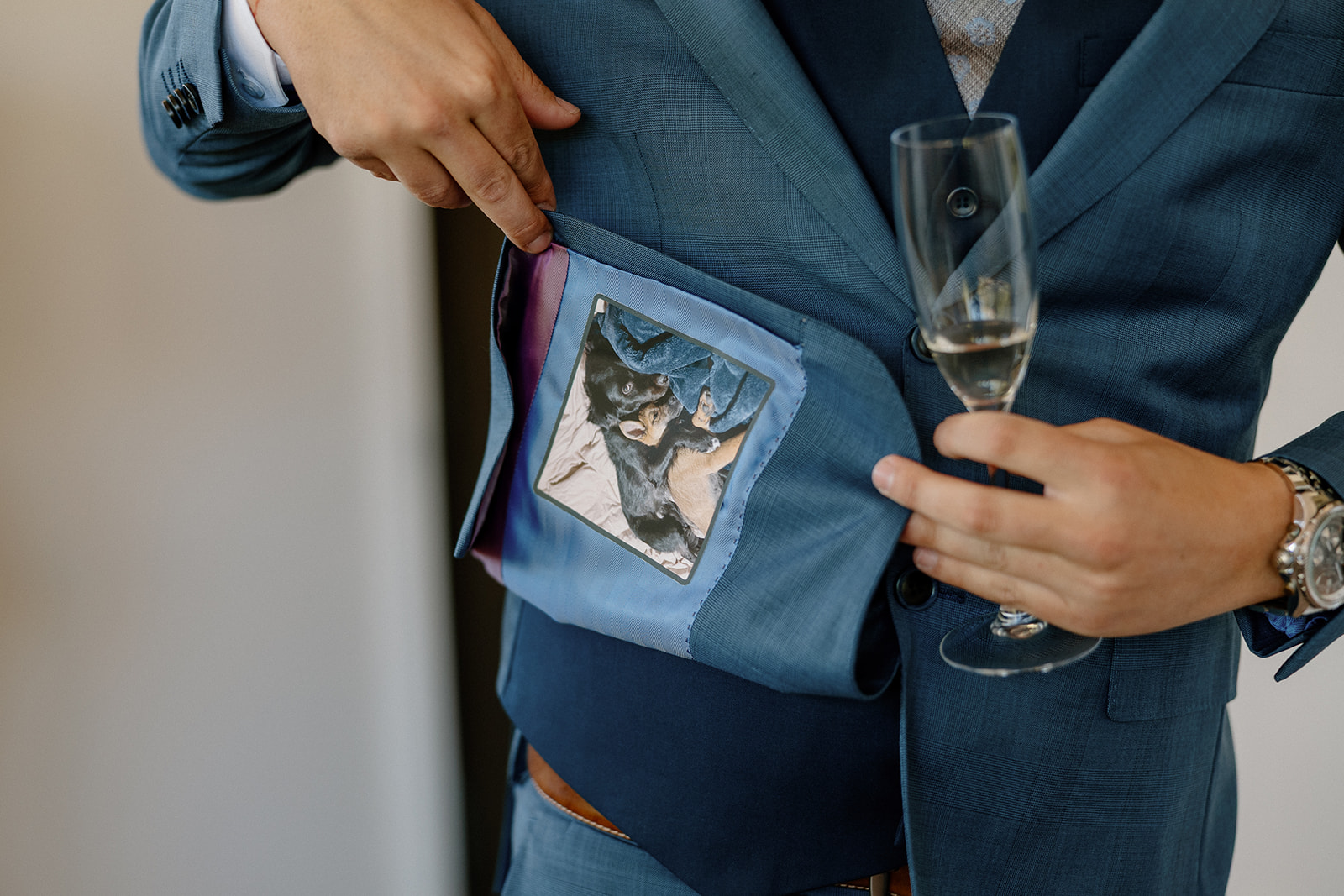 The groom reveals a custom suit lining featuring a photo of his dog, holding a glass of champagne with a proud smile.