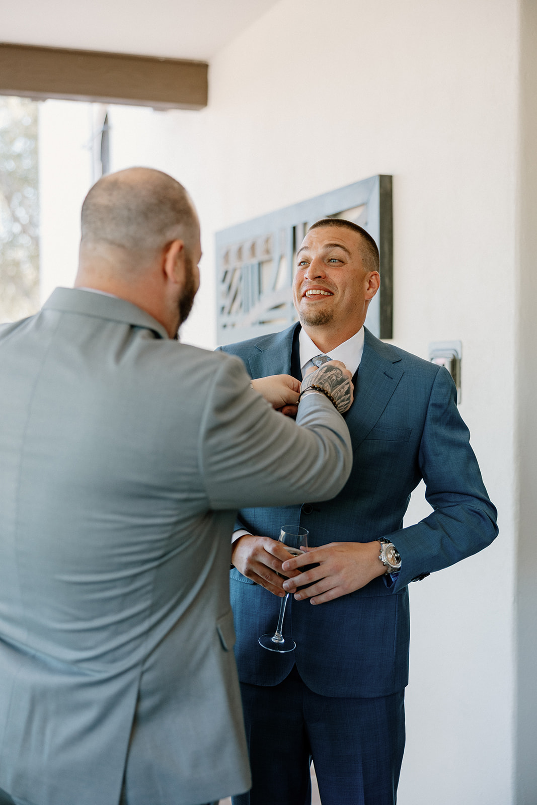 One of the groomsmen fixes the groom’s tie before the ceremony, capturing a laid-back, supportive moment.