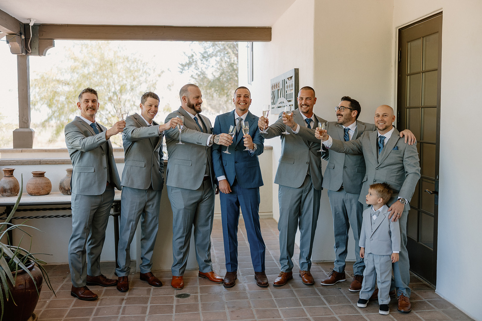 The groom and his groomsmen raise a celebratory toast while the tiniest suited VIP steals the spotlight.