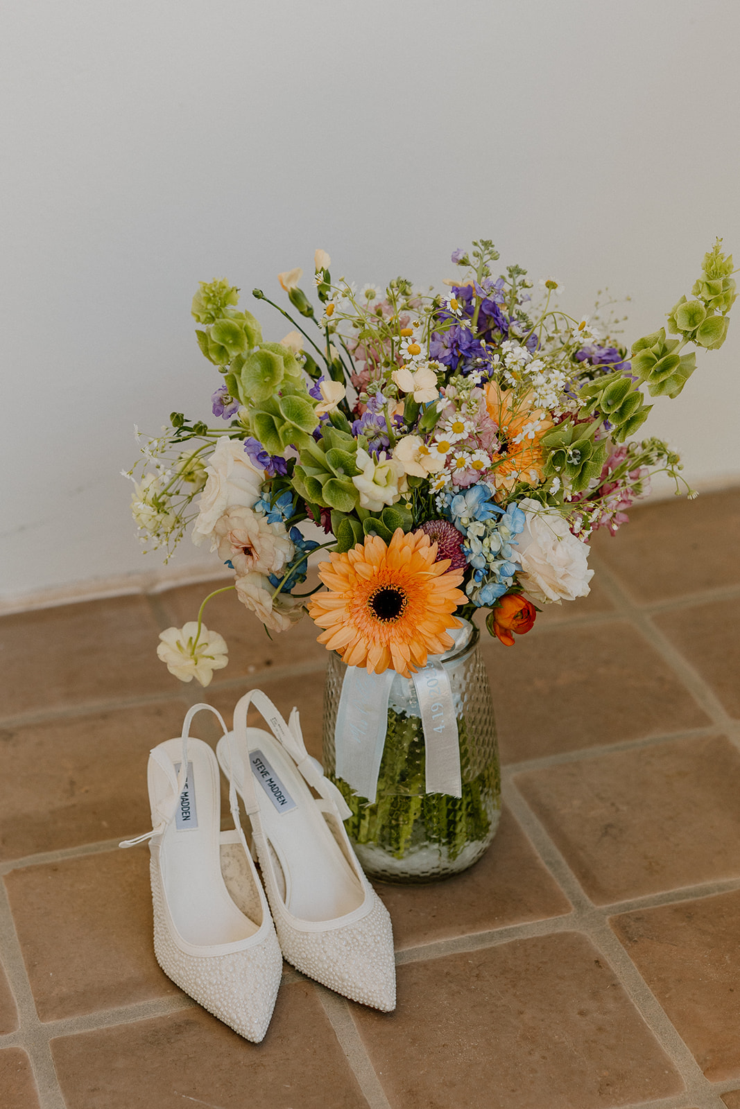 White heels sit beside a vibrant wildflower bouquet, styled against a rustic tile floor for the ultimate desert-romantic flatlay.