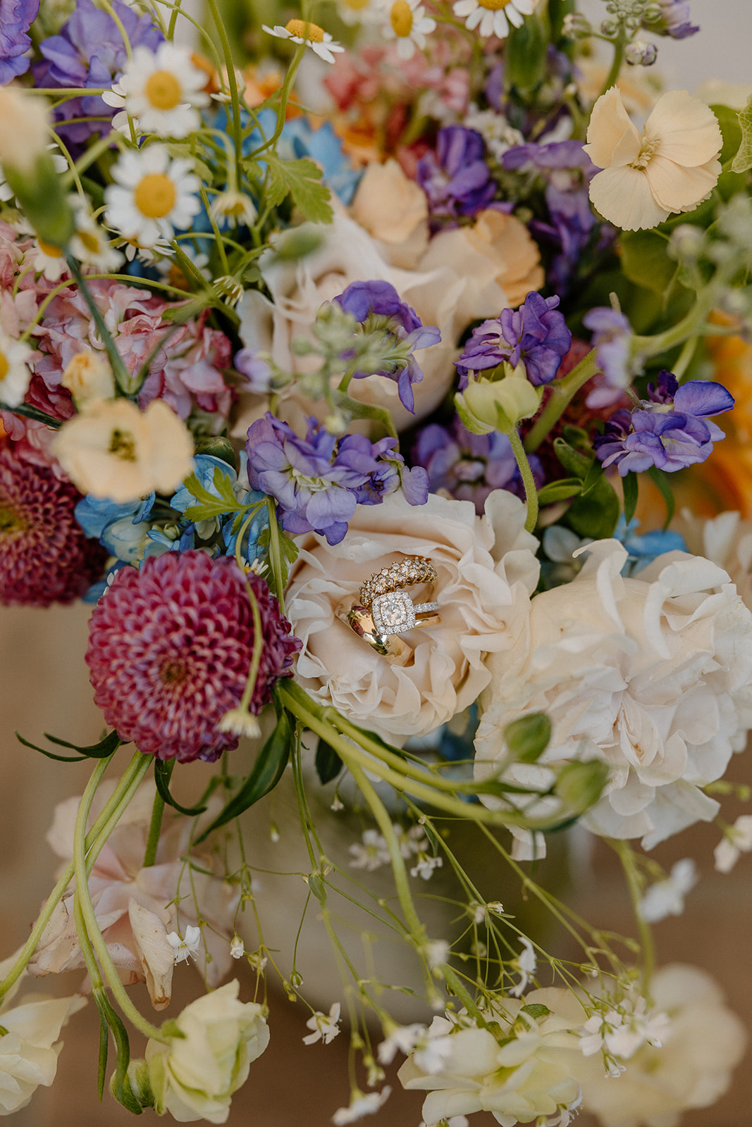 Wedding rings tucked into a dreamy floral bouquet, nestled among pastel petals and delicate textures.