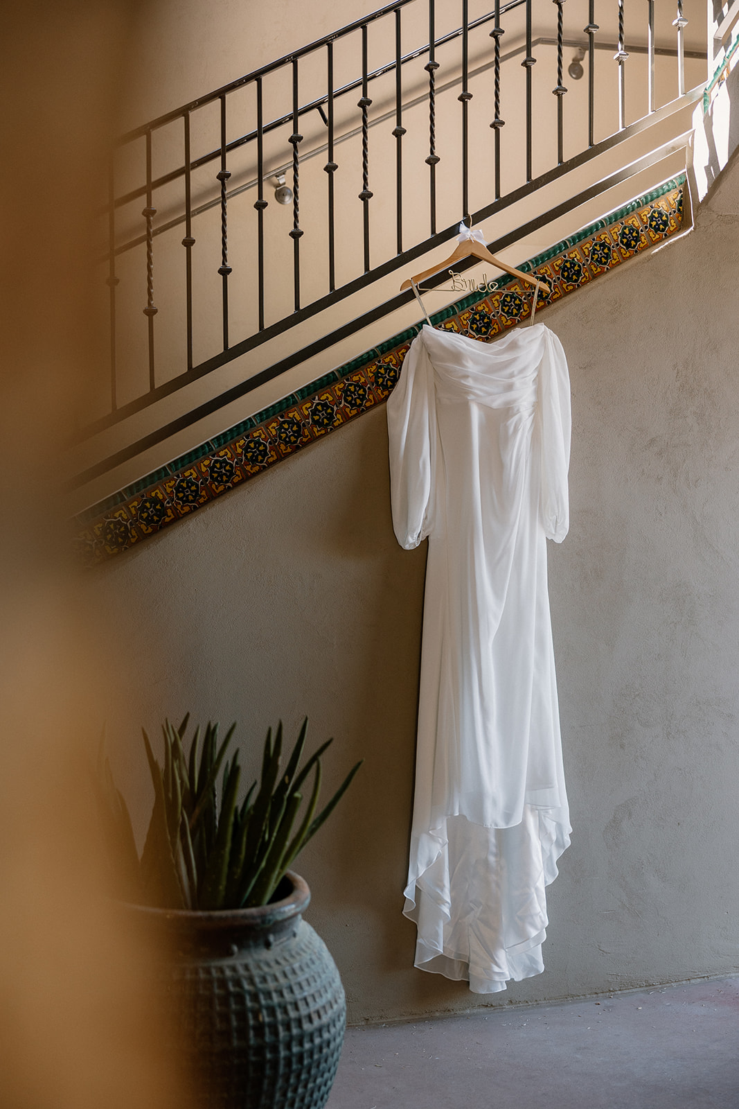 The bride’s long-sleeved gown hangs from the staircase at Blackstone Country Club, catching the soft glow of morning prep.