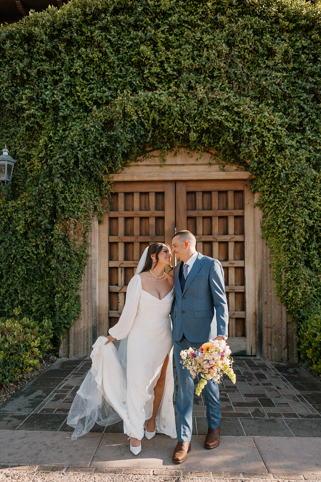 The bride and groom share a quiet moment in front of the iconic ivy-covered wooden doors at Blackstone Country Club, bouquet in hand and smiles all around.