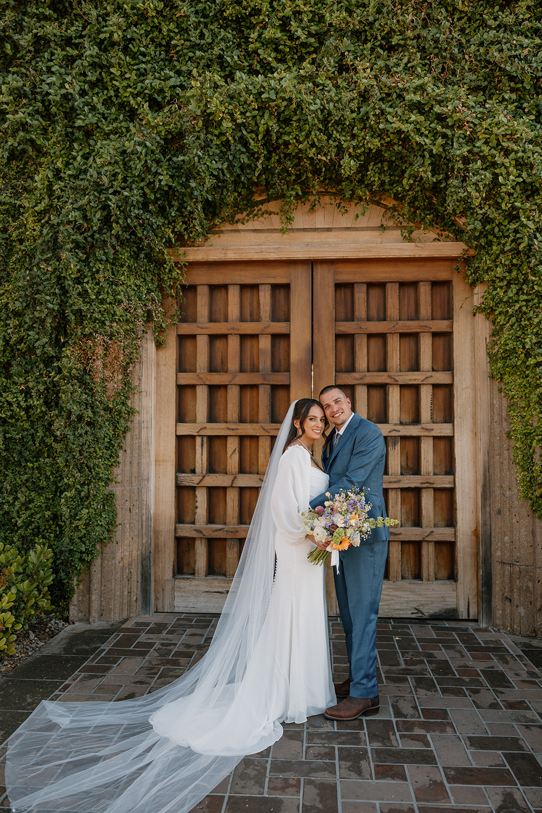 The bride and groom snuggle up in front of the iconic wooden doors and ivy wall at Blackstone Country Club, veil flowing behind them.