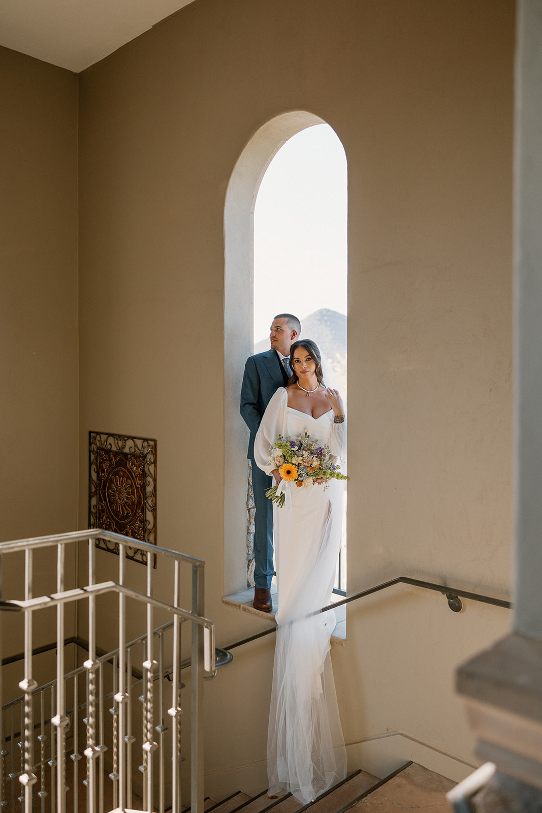 Moody and romantic stairwell moment at Blackstone Country Club, with the couple framed by a tall arched window.