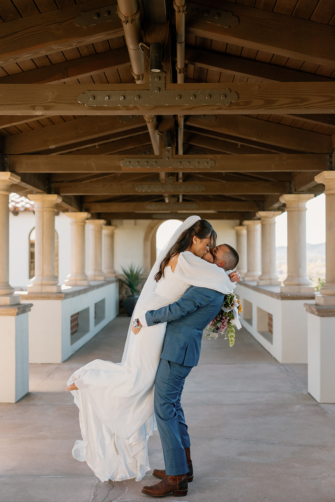 The groom lifts the bride in a joyful kiss under the arched breezeway at Blackstone Country Club, just after their first look.