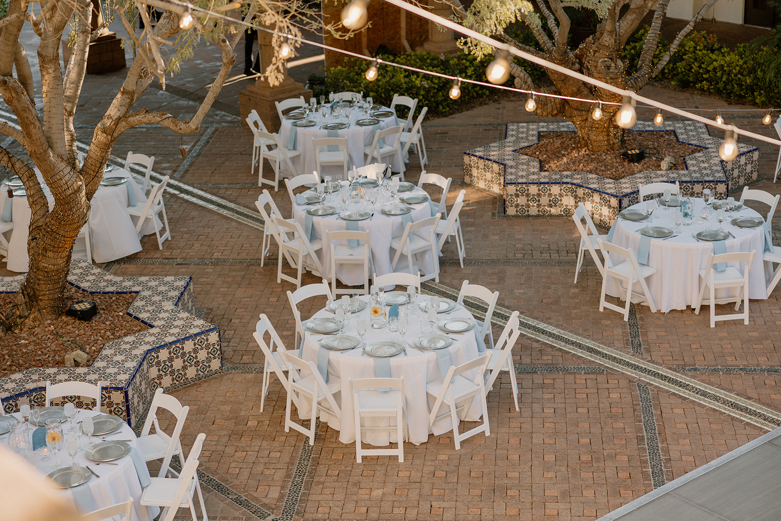 Golden hour light spills over the courtyard reception tables at Blackstone Country Club, with bistro lights and tiled tree planters completing the scene.